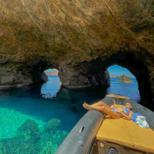 The dramatic rocky coastline and hidden sea caves of Tragonisi island, a breathtaking and secluded alternative to the typical Mykonos beaches.