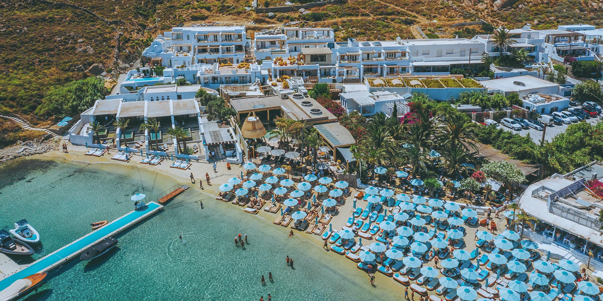 Drone view of Psarou beach and famous Mykonos restaurants by boat