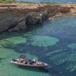 A Don Blue Yachting RIB anchored at a secluded rocky cove on the north coastline of Paros, guests enjoying the crystal clear turquoise waters - one of the best beaches in Paros only reachable by boat