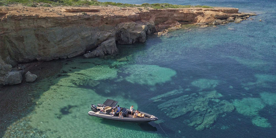 A Don Blue Yachting RIB anchored at a secluded rocky cove on the north coastline of Paros, guests enjoying the crystal clear turquoise waters - one of the best beaches in Paros only reachable by boat