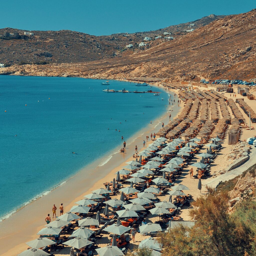 A drone photograph captures the density of sunbeds on a popular Mykonos coast, illustrating the choice between Mykonos sunbed prices vs private boat comfort.